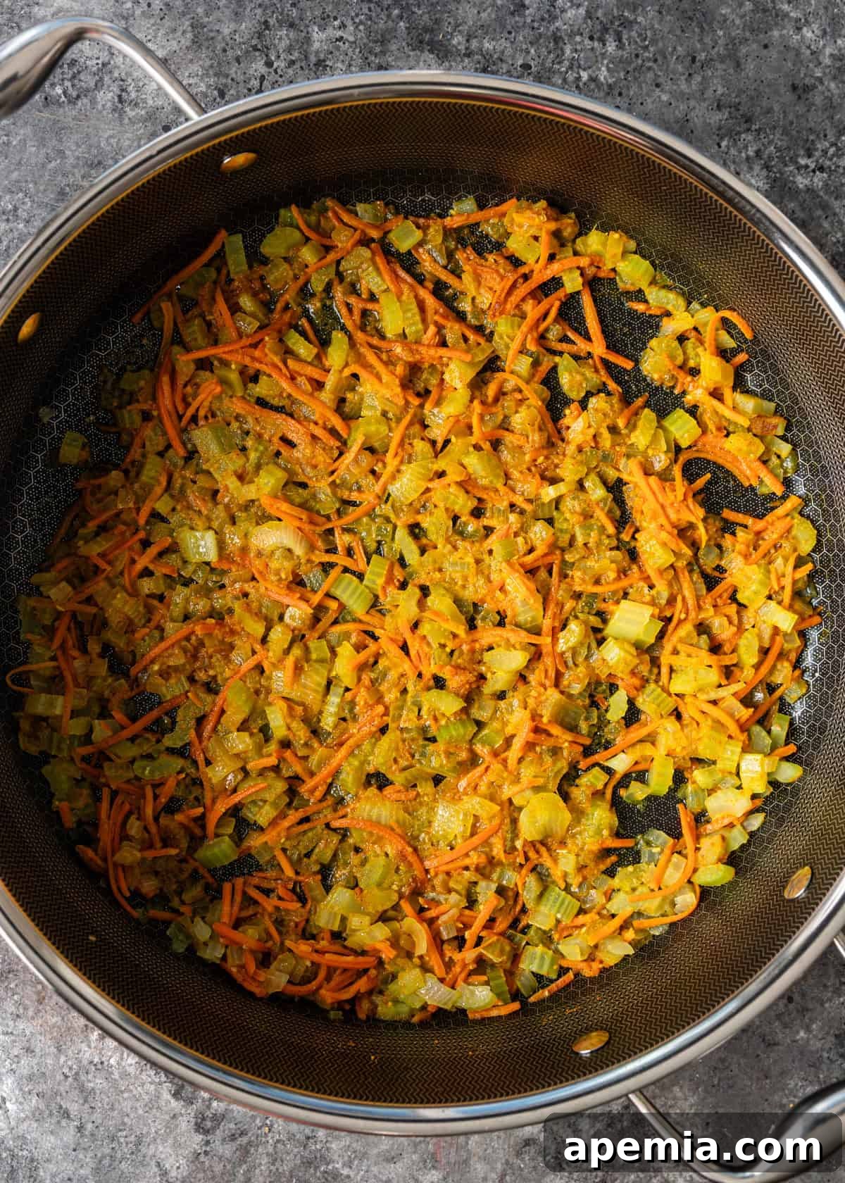 Overhead process shot of chopped onions, carrots, celery, and aromatic spices sautéing in a Dutch oven pan.