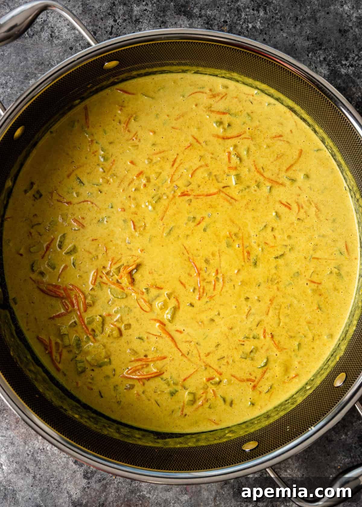 Overhead process shot showing sautéed vegetables with coconut milk and peanut butter added to the Dutch oven, being stirred to create the creamy curry base.