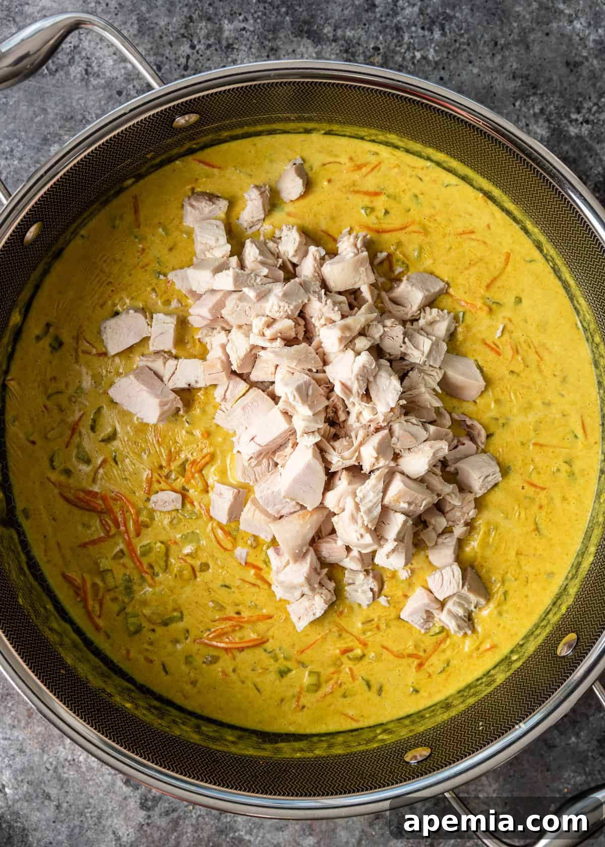 Overhead process shot illustrating cooked chicken being added to the rich coconut milk and peanut butter sauce with vegetables in the Dutch oven.