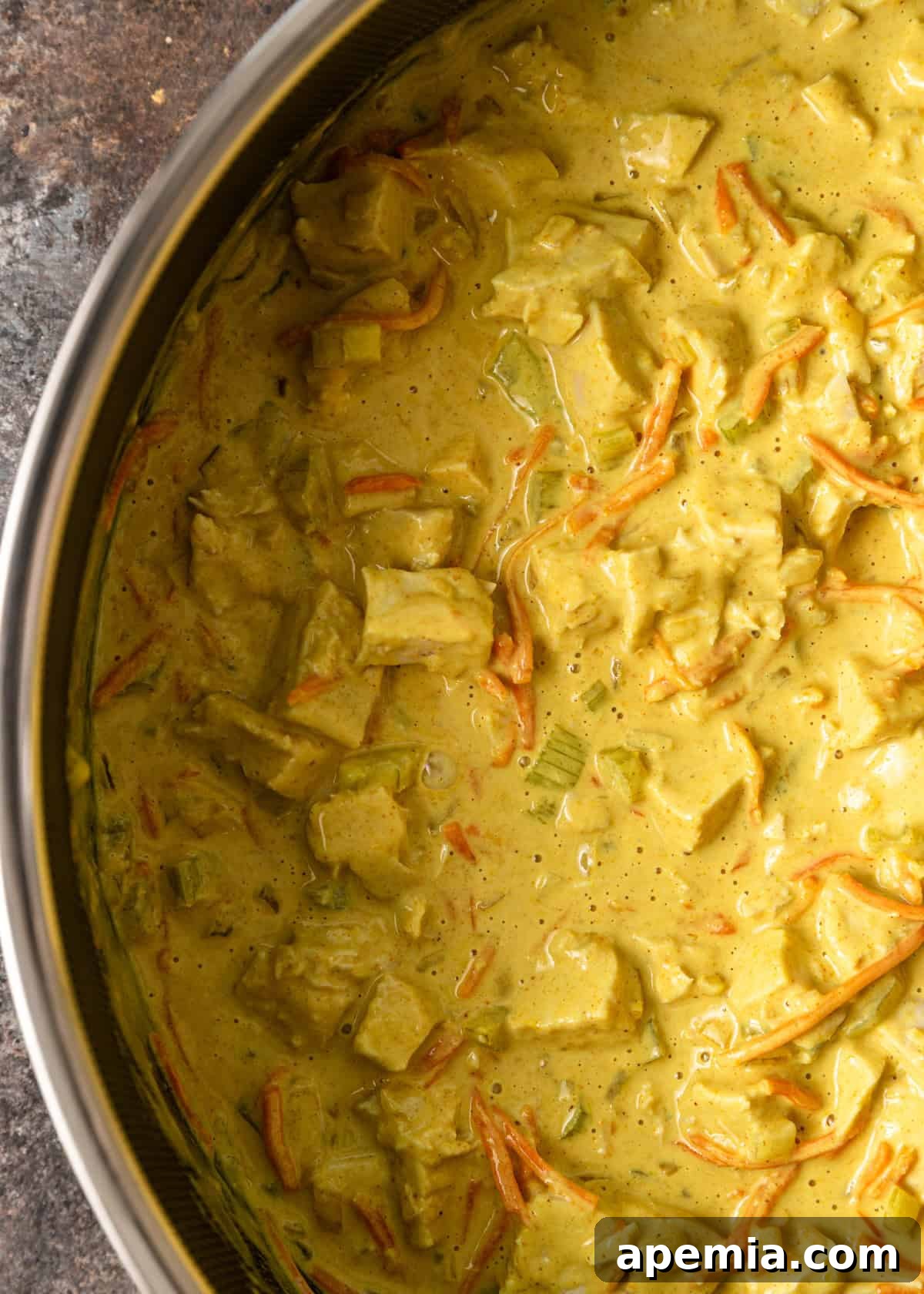 Closeup overhead view of the fully cooked chicken peanut curry simmering in a Dutch oven, with its thick, creamy sauce and vibrant ingredients.