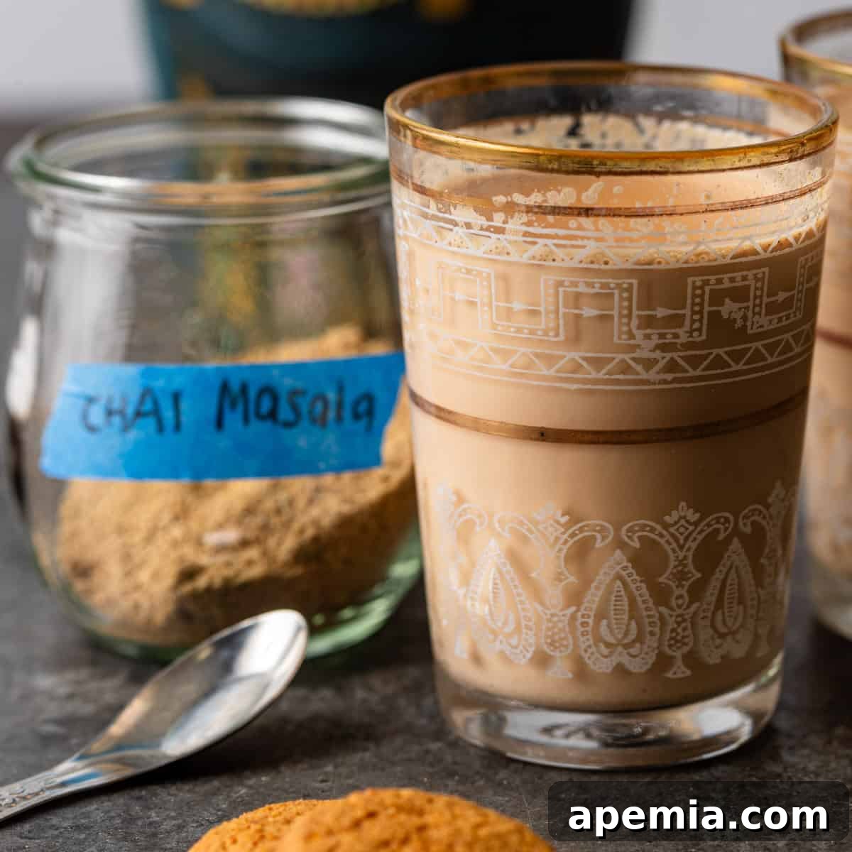 closeup side view: cup of masala chai with chai masala spices in jar and spoon on counter