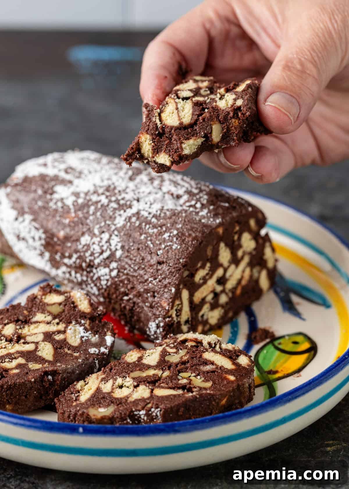 closeup side view: hand holding slice of chocolate salami over plate