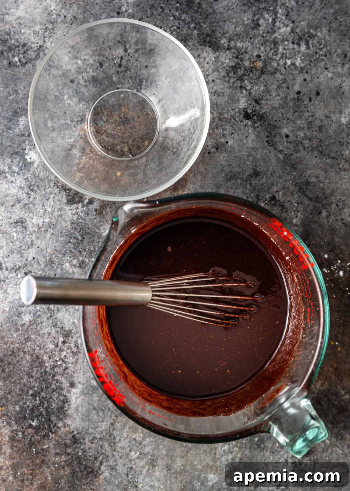 overhead process shot: empty bowl besides measuring cup holding chocolate mixture and whisk