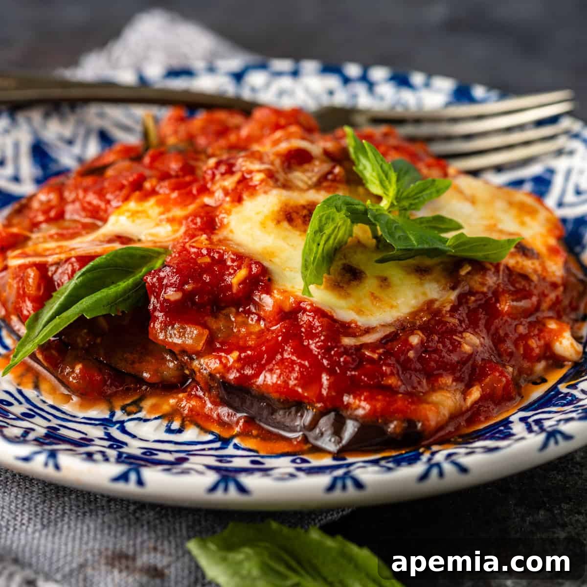 closeup side view: eggplant parmigiana on blue and white plate with fork