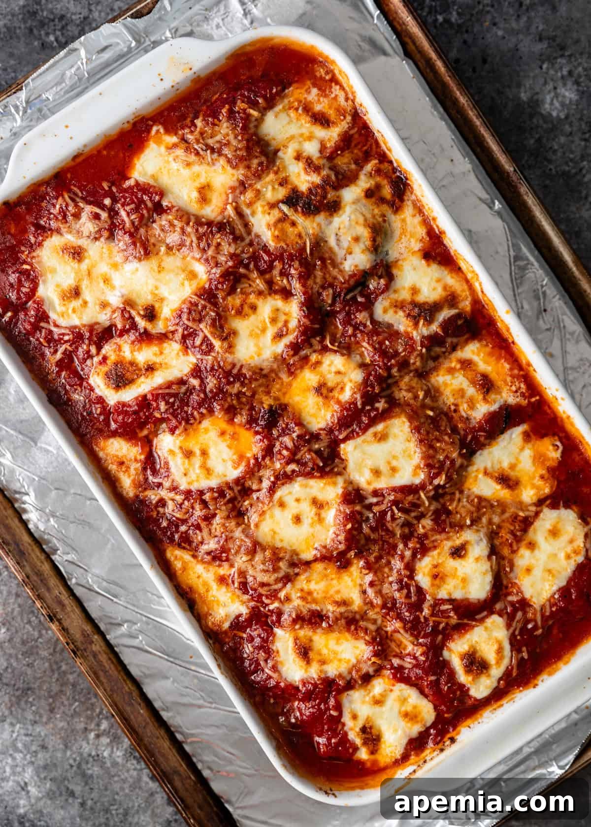 overhead process shot: baked eggplant parmigiana on cooking sheet ready to serve