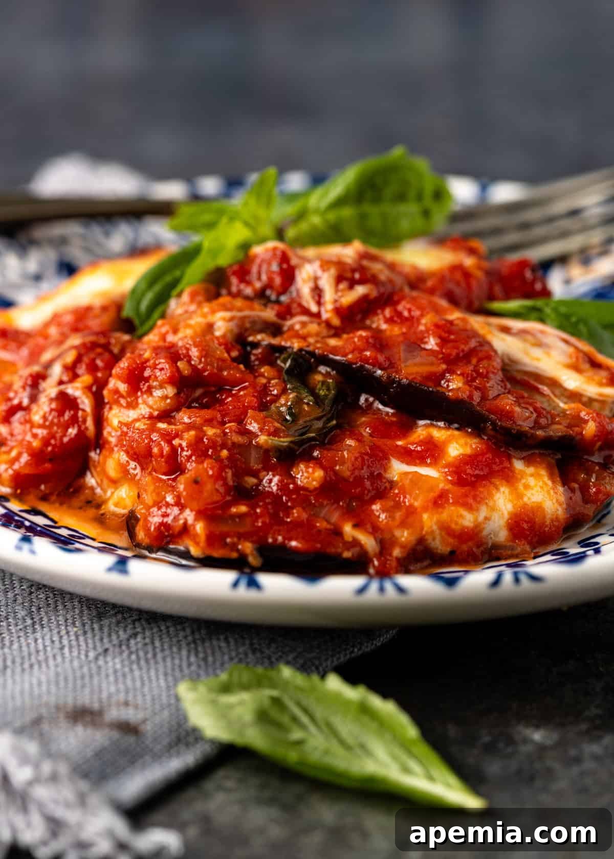 closeup side view: eggplant parmigiana on white and blue plate ready to eat