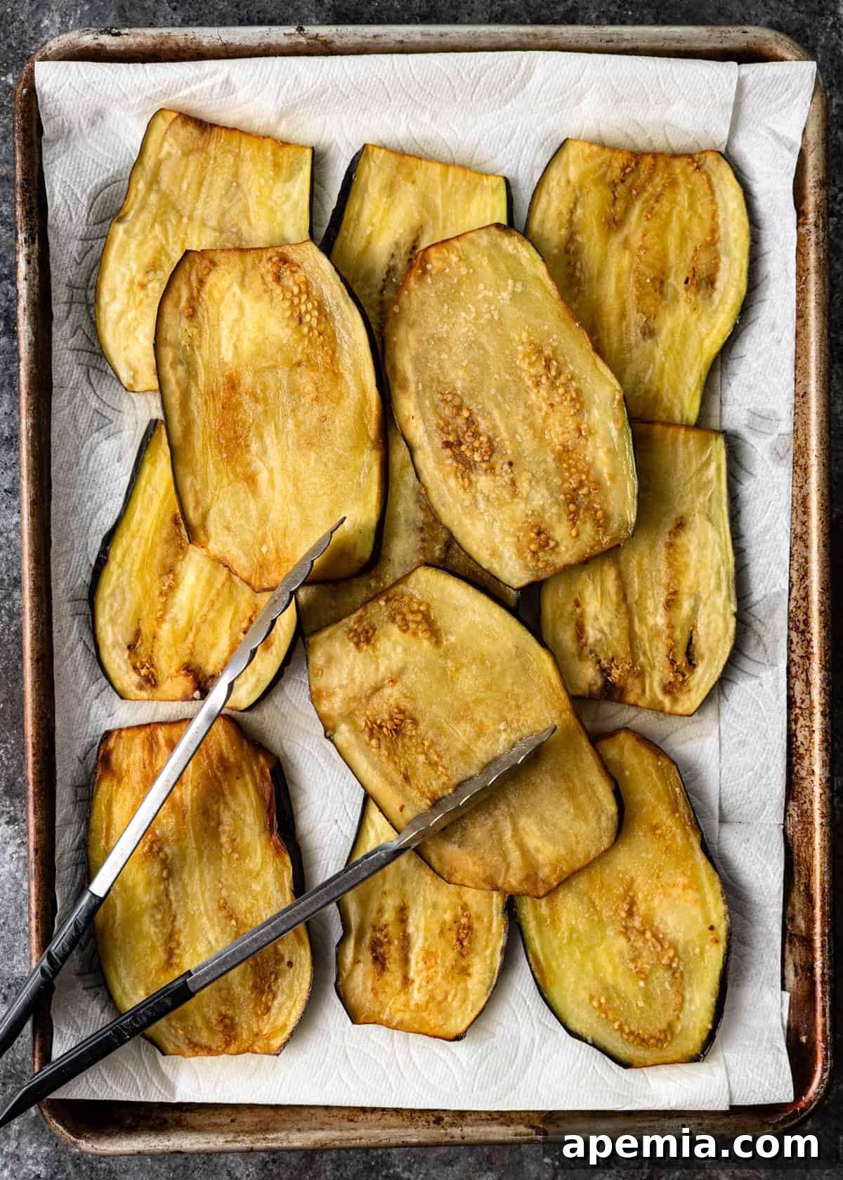 overhead process shot: fried eggplant on baking sheet with tongs on top