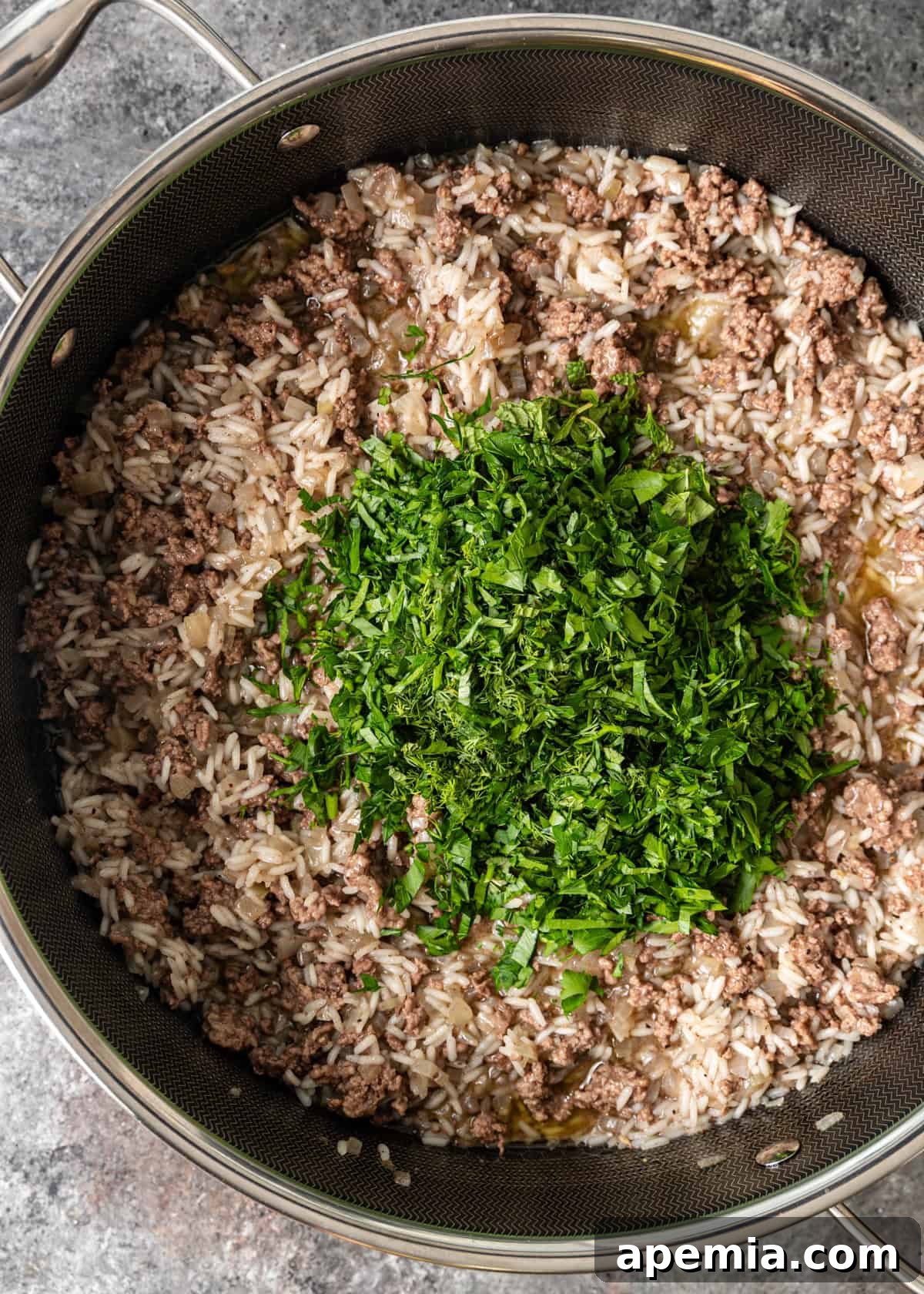overhead process shot: herbs being folded into rice, ground beef and onions in deep skillet