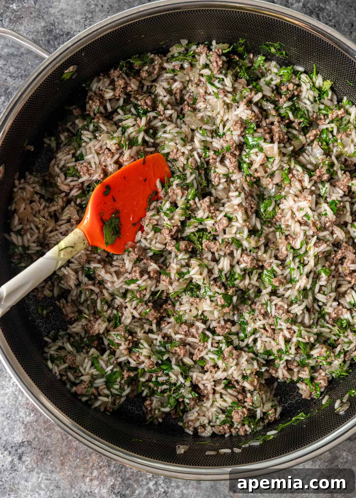 overhead process shot: herbs being folded into rice, ground beef and onions in deep skillet with spatula