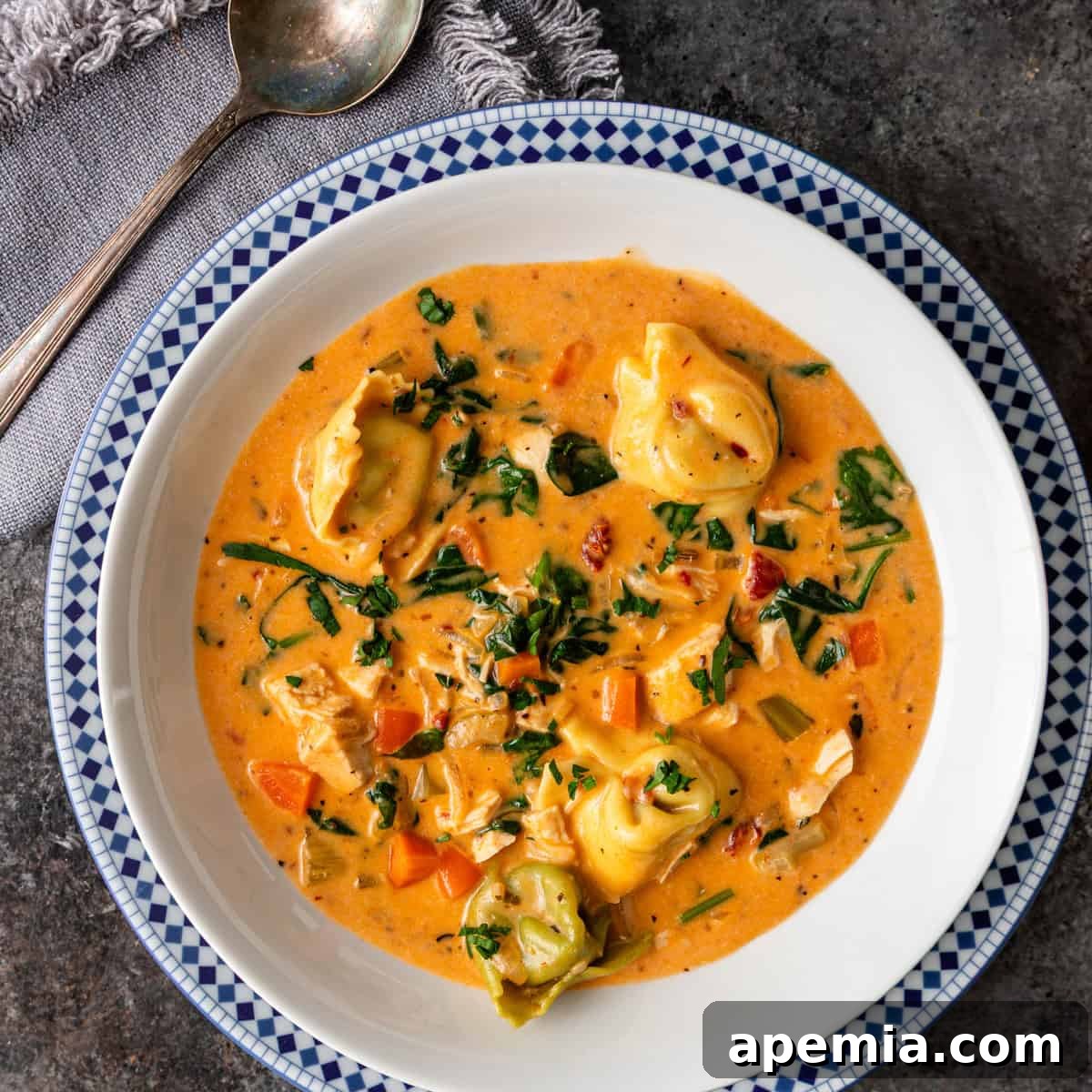 Overhead shot of a bowl of creamy Tuscan tortellini soup, garnished with fresh herbs, resting on a rustic kitchen counter.