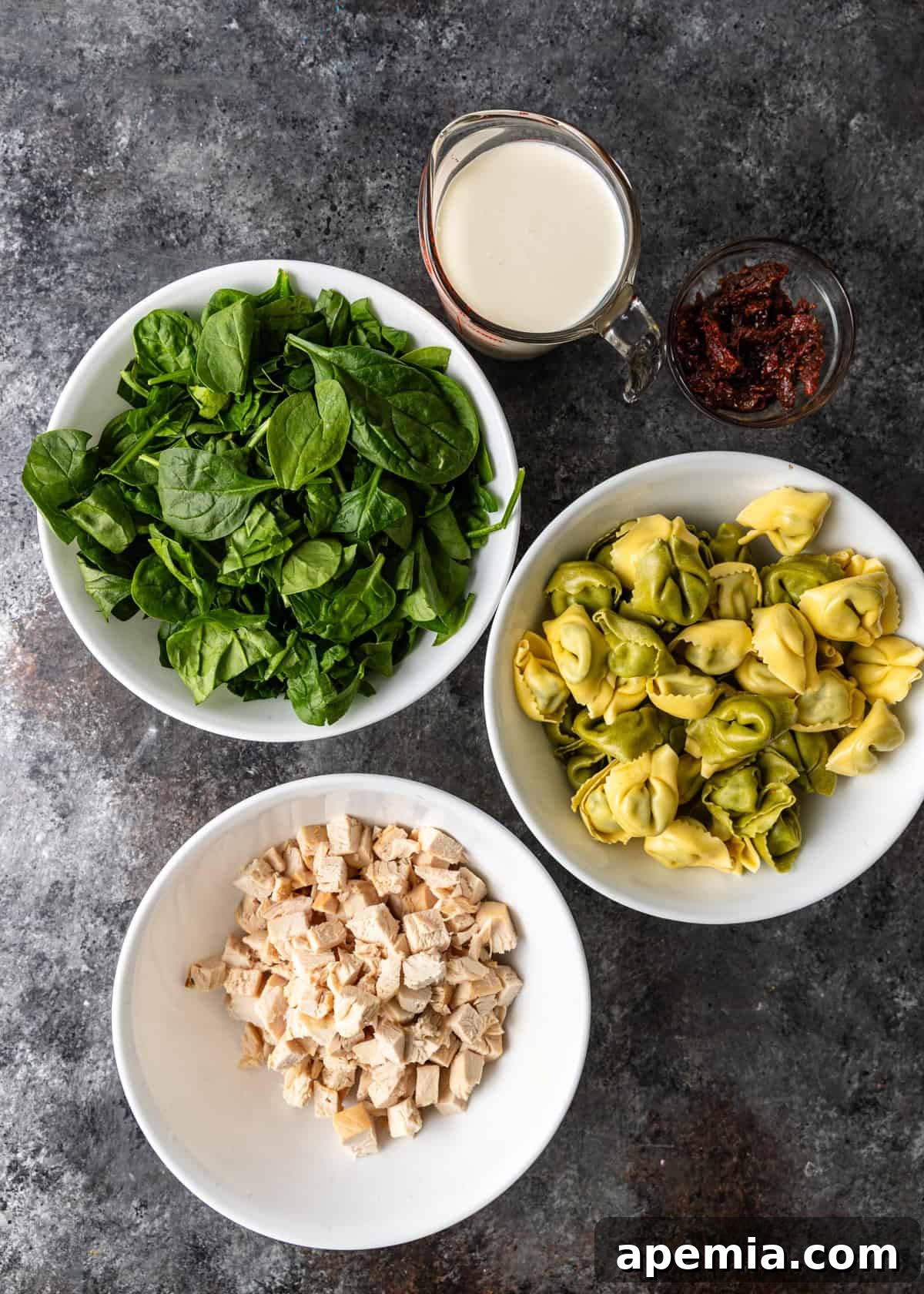 Overhead process shot showing all the main ingredients ready for cooking the tortellini soup recipe, including chicken, pasta, and vegetables.