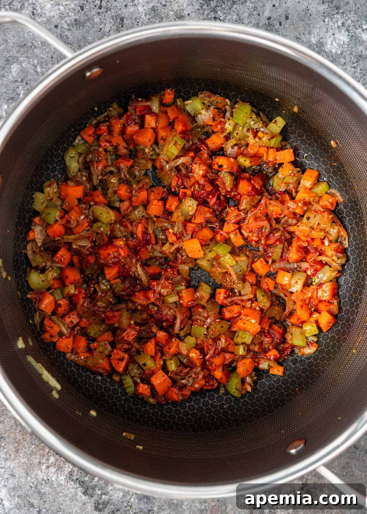 Overhead view of finely diced onion, celery, and carrots sautéing in a large stockpot, forming the aromatic base of the soup.