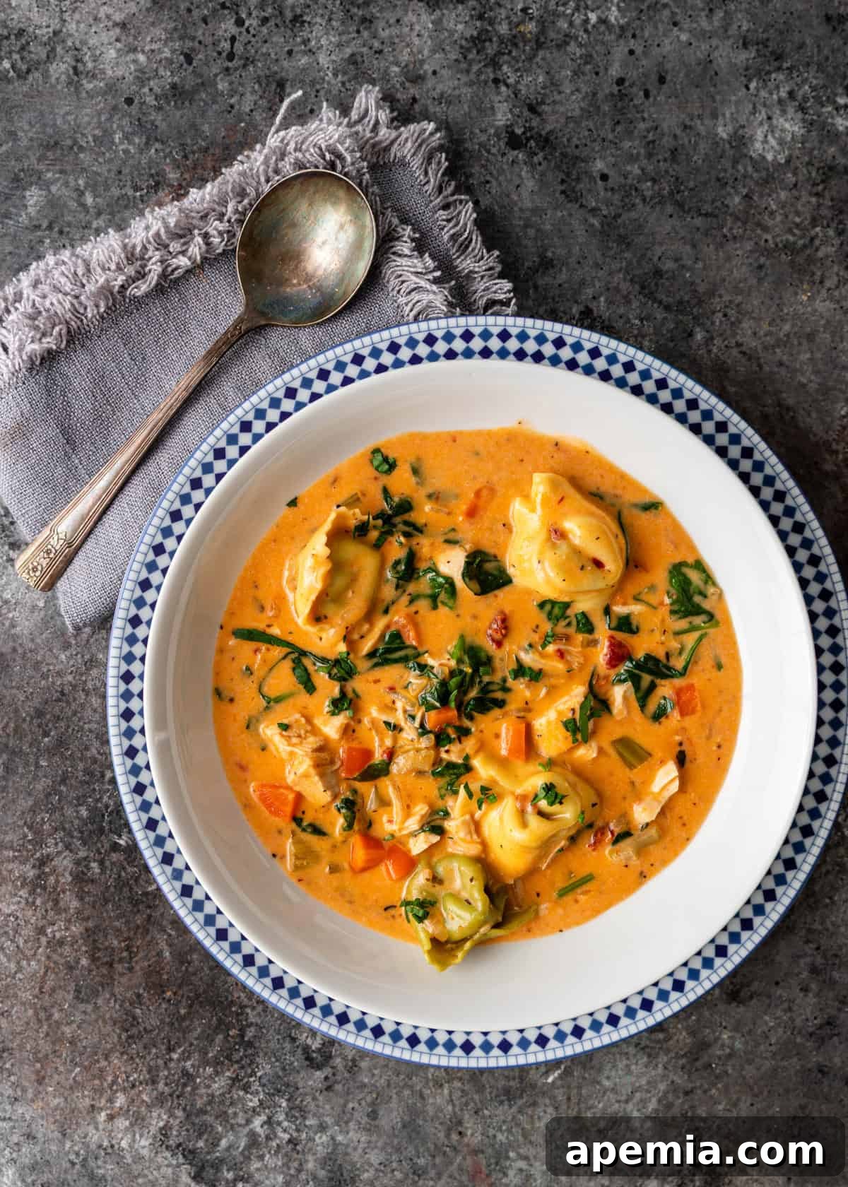 Overhead shot of a bowl of creamy Tuscan tortellini soup on a kitchen counter, with a spoon resting to the side, ready to be enjoyed.