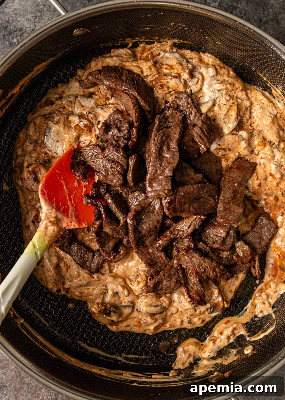 overhead process shot: cooked sliced meat added to the diced onions and sliced mushrooms in skillet