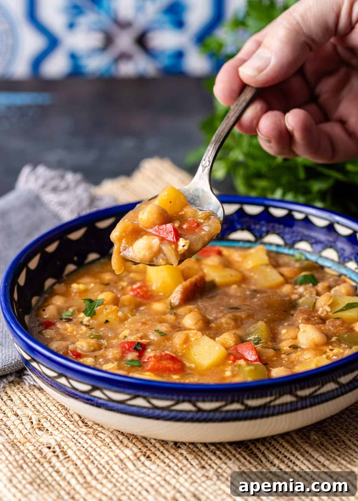 closeup side view: spoonful of Spanish chickpea stew over white and blue bowl of chickpea stew