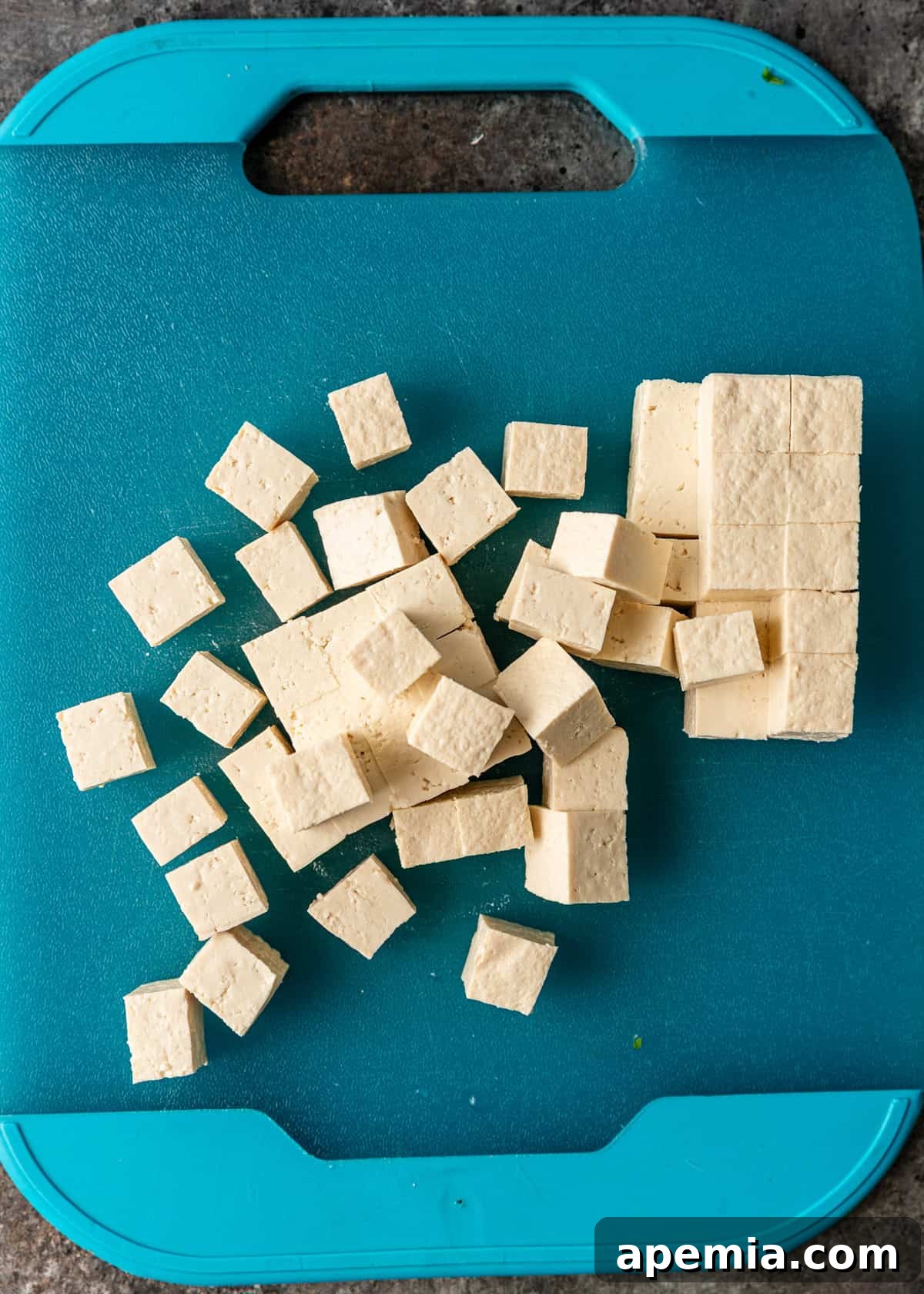 overhead process shot: tofu being cut into 1-inch thick slabs on blue cutting board