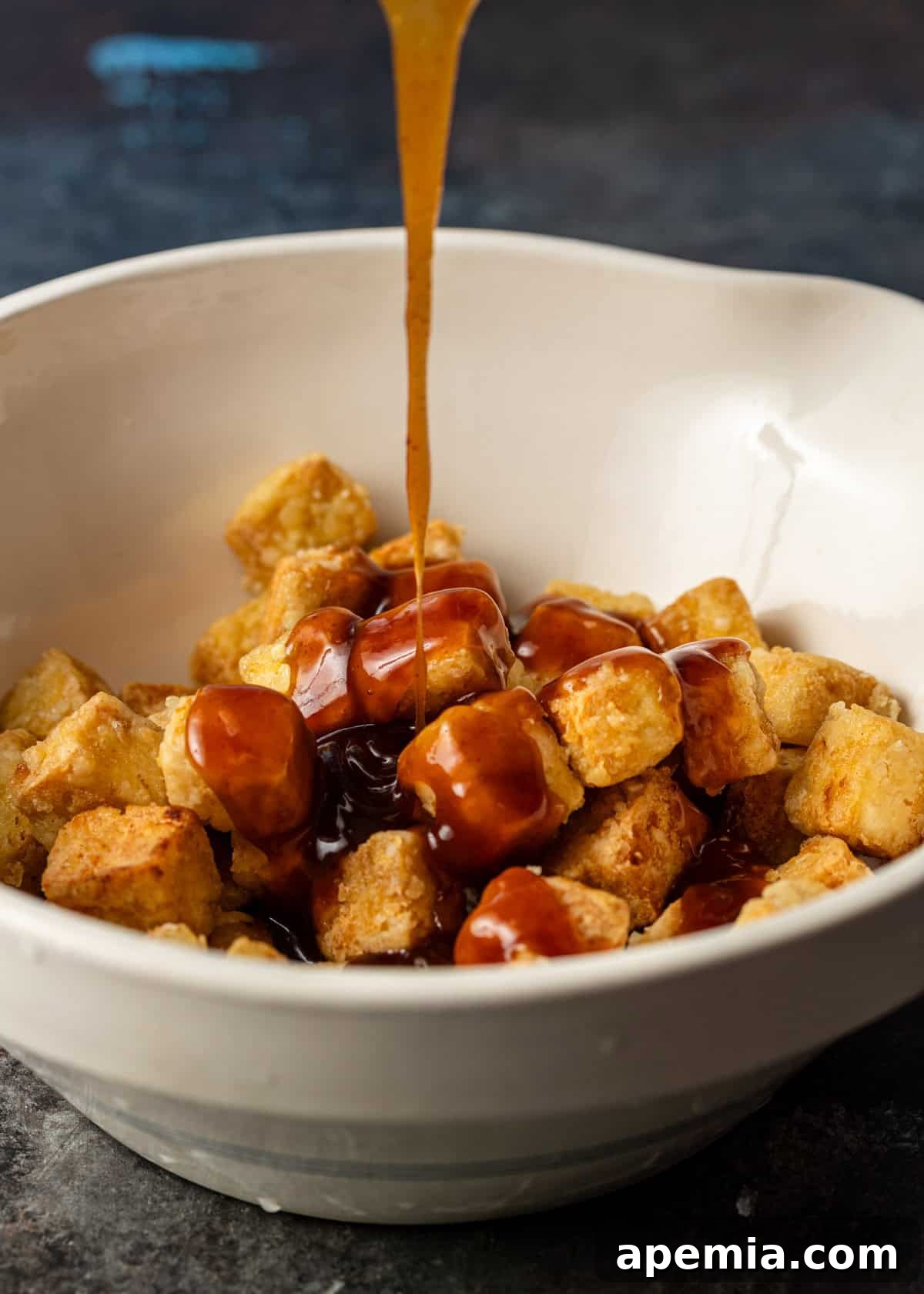 closeup side view: honey sauce being poured on tofu in white bowl