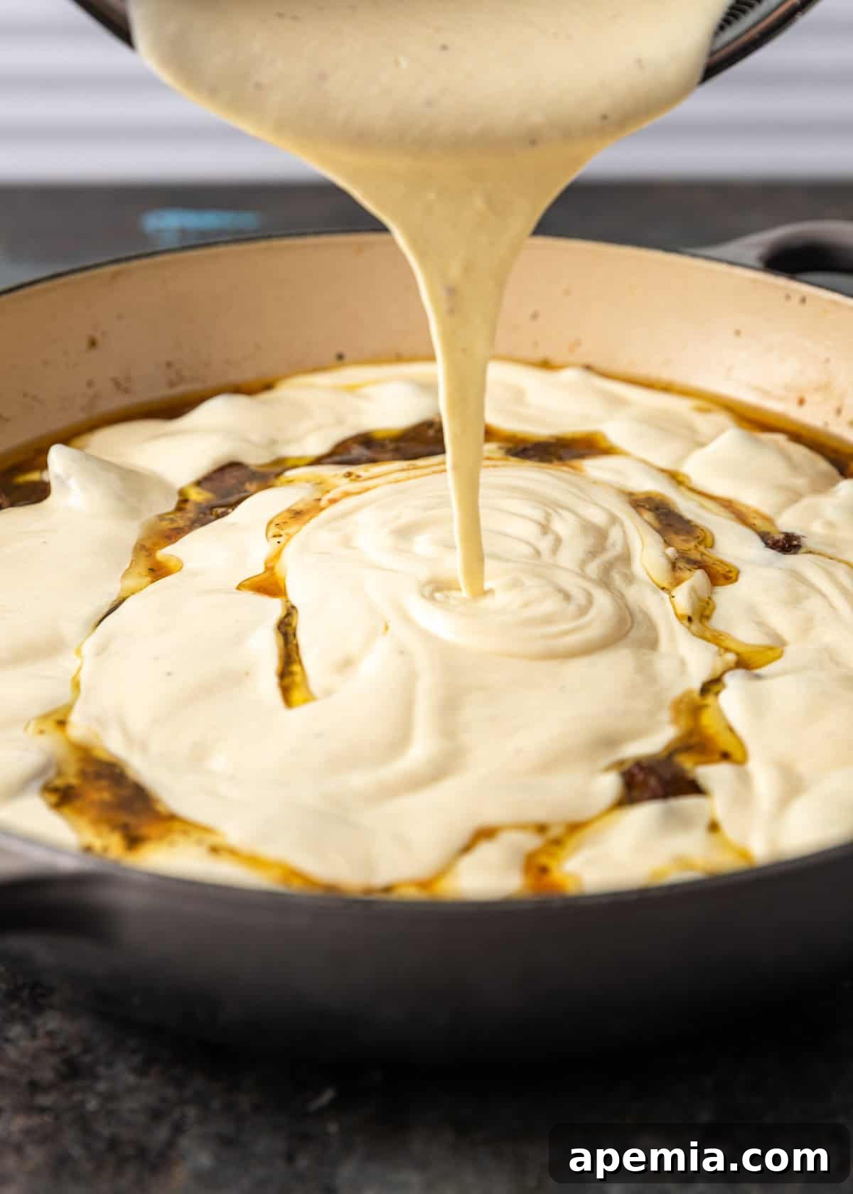 closeup side view: sauce being poured on top of cooked lamb cubes in skillet
