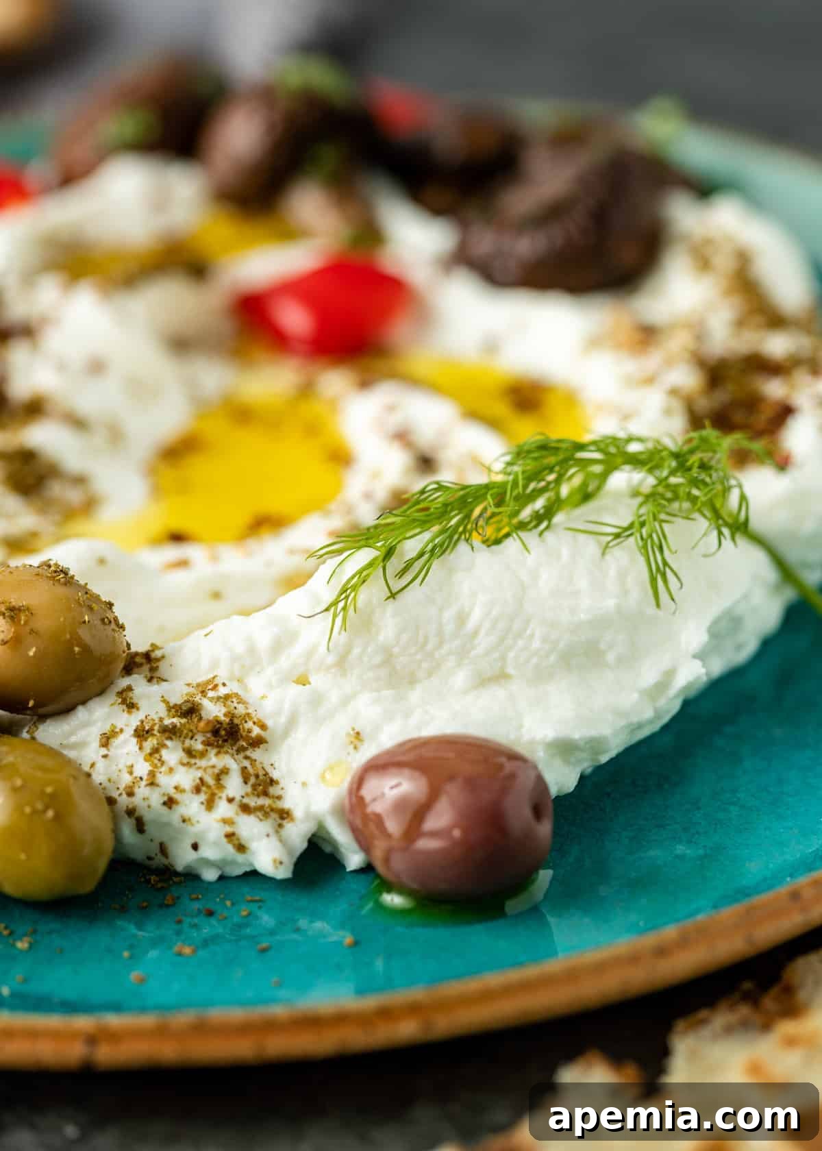 Extreme close-up of labneh topped with a delicate drizzle of olive oil, surrounded by vibrant green olives