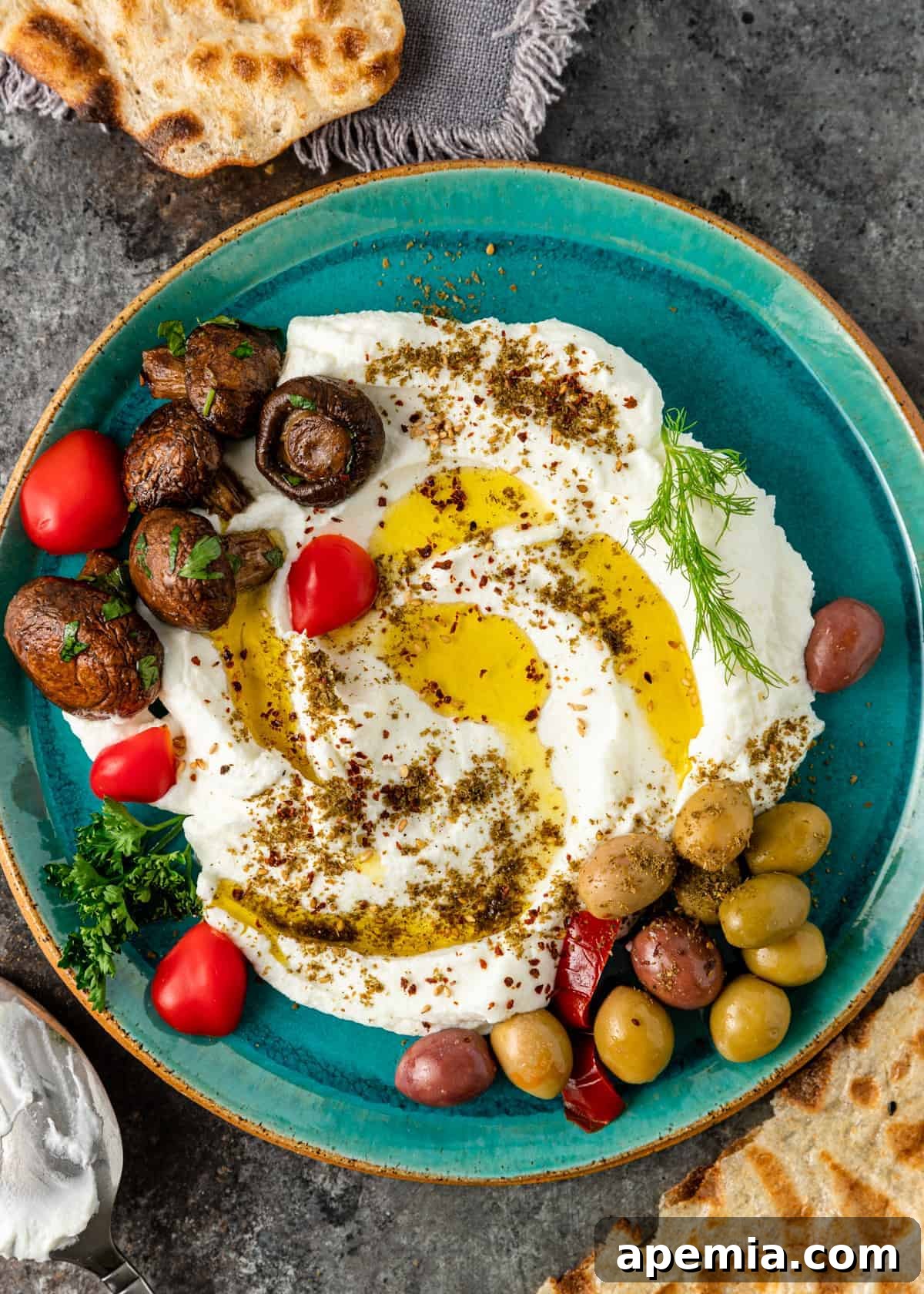 Top-down view of a platter of homemade labneh garnished with marinated mushrooms, olives, and cherry tomatoes