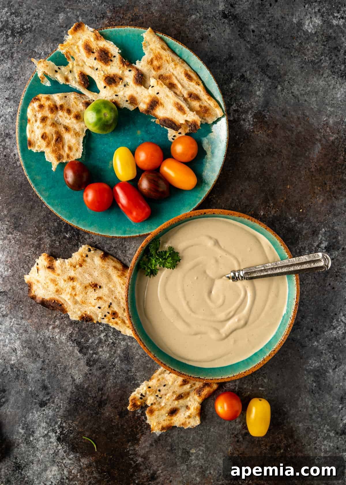 overhead of a bowl of tahini sauce with pita and tomatoes for dipping