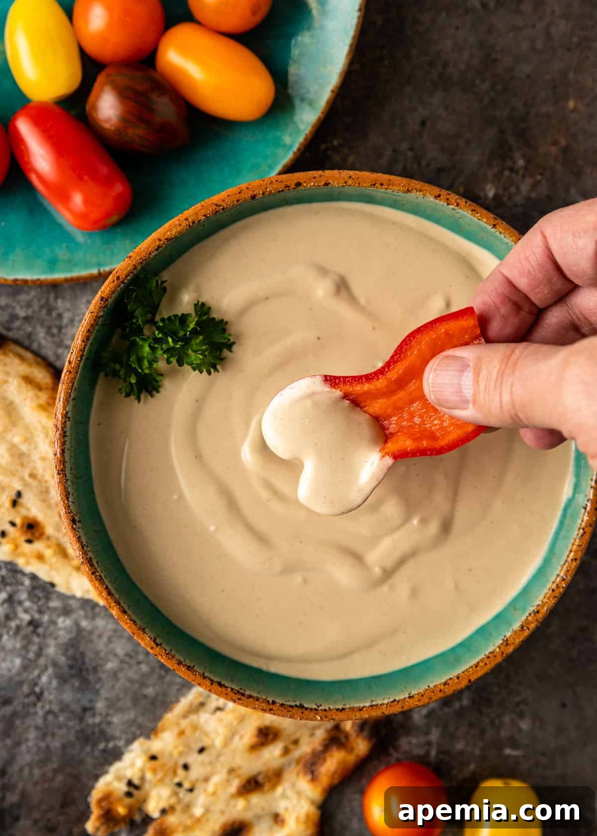overhead of red bell pepper being dipped into a bowl of tahini sauce
