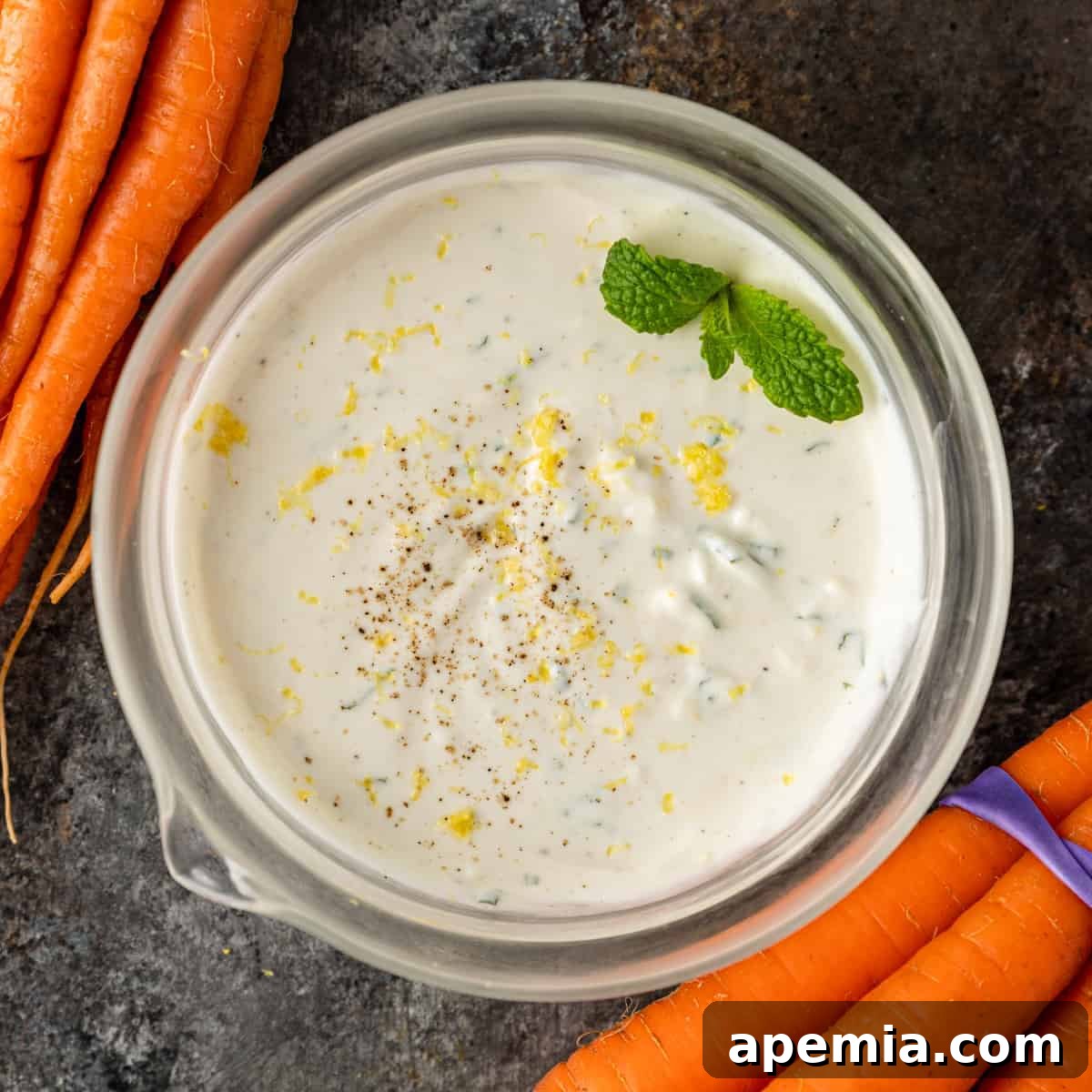 overhead image: creamy tahini yogurt sauce in clear glass bowl garnished with a mint sprig and lemon zest