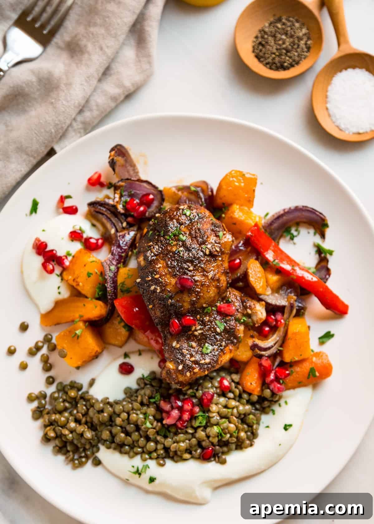 North African spiced roast chicken on a white plate with roasted vegetables and lentils, garnished