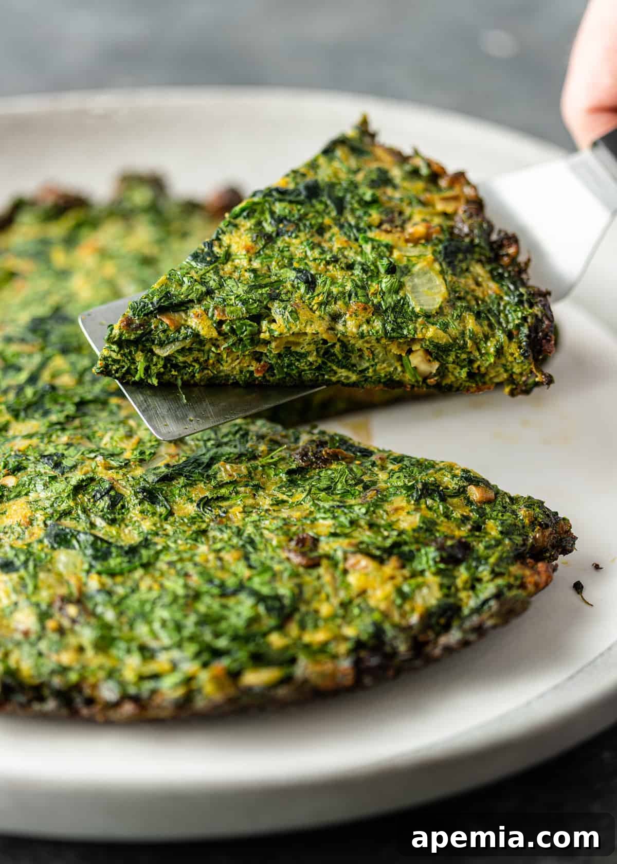 A perfectly golden-brown slice of Persian Kuku Sabzi being lifted from the pan with a spatula, revealing its rich green interior.