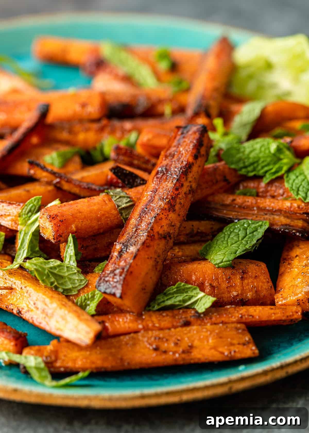 Close-up shot of a plate elegantly stacked with tender, beautifully spiced Moroccan roasted carrots, highlighting their caramelized edges and fresh mint garnish.