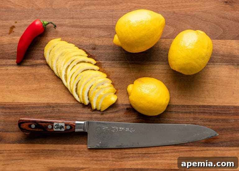 Three whole lemons and a chef's knife resting next to thinly sliced lemon pieces on a wooden cutting board, illustrating the preparation stage.