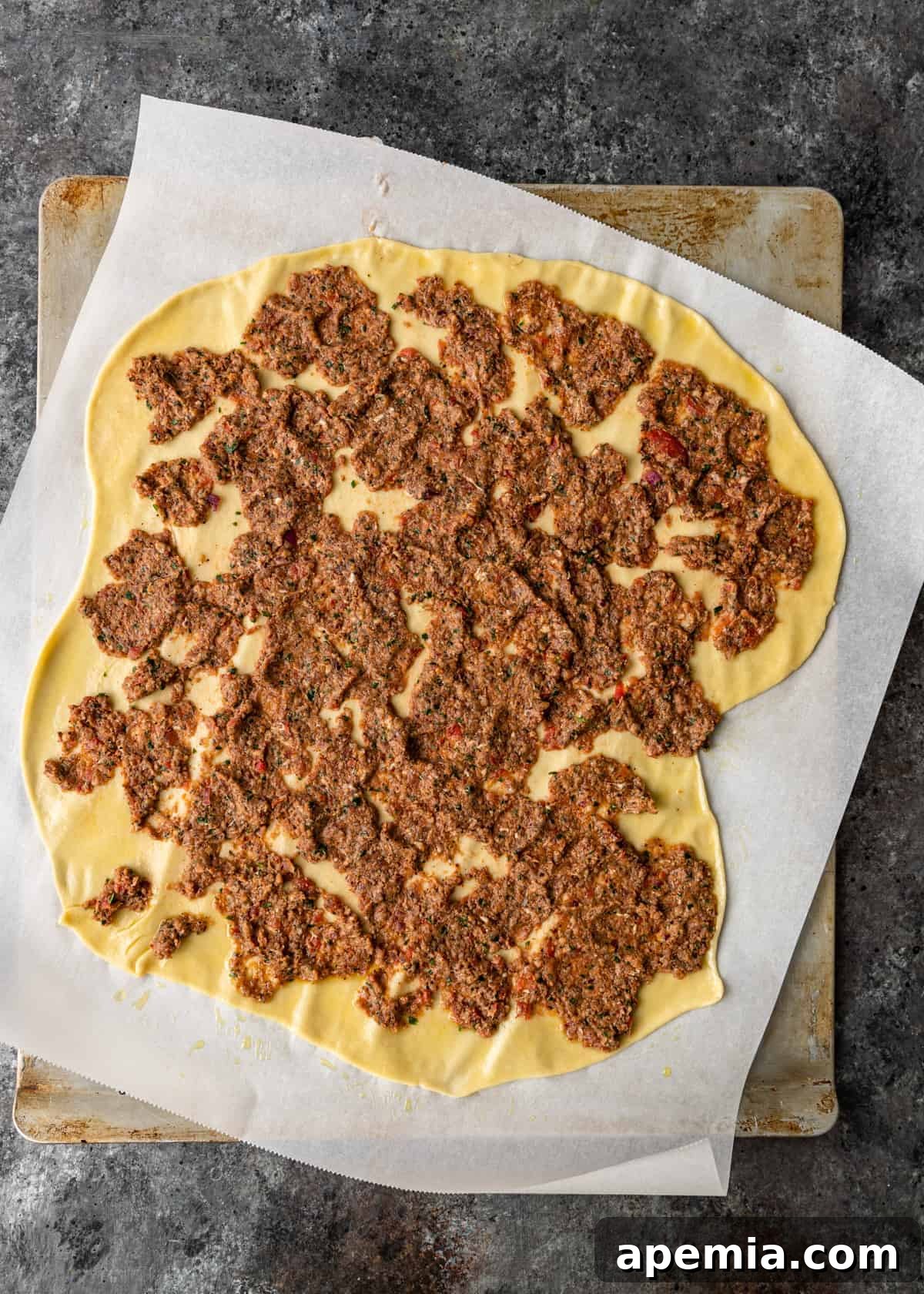 overhead: lahmacun flatbread pizza on parchment paper, ready for baking