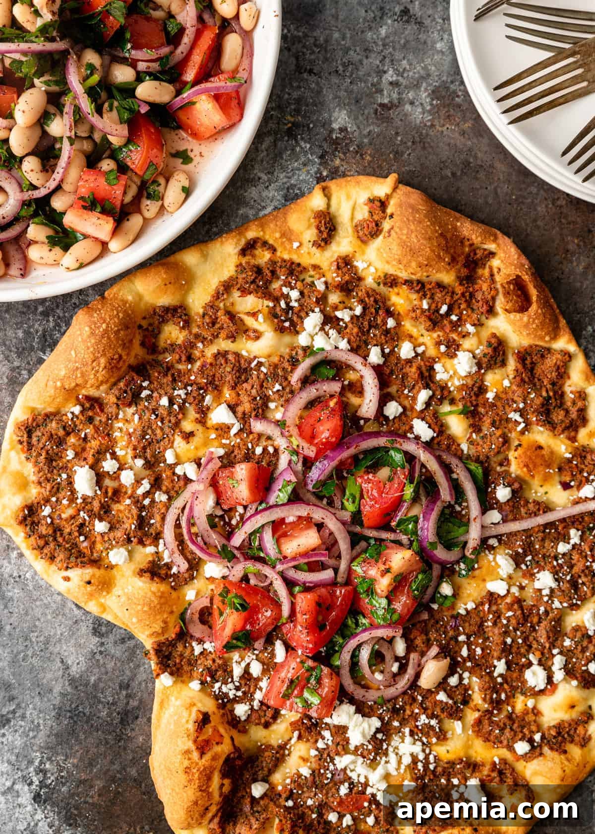 overhead: baked lahmacun topped with red onion, tomatoes, basil, and feta cheese