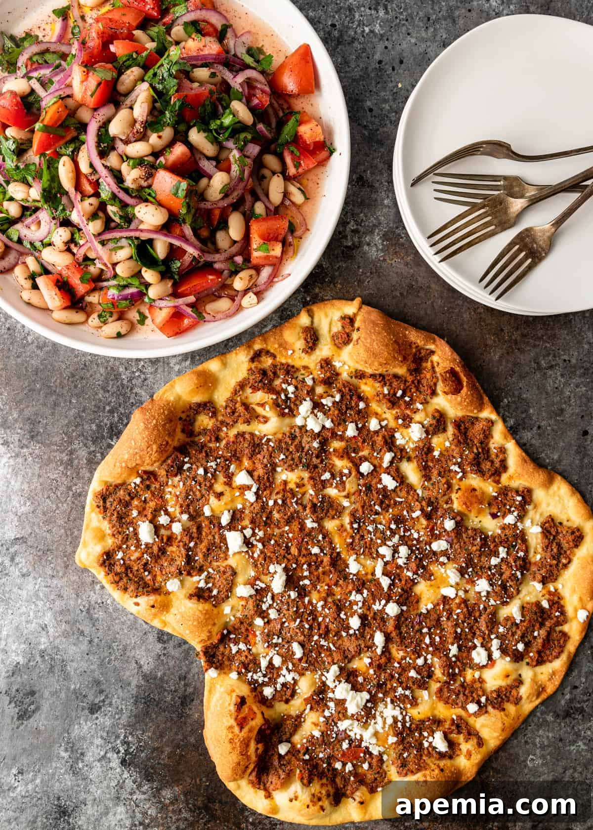 overhead: turkish pizza next to bowl of 4 bean salad, serving plates and forks