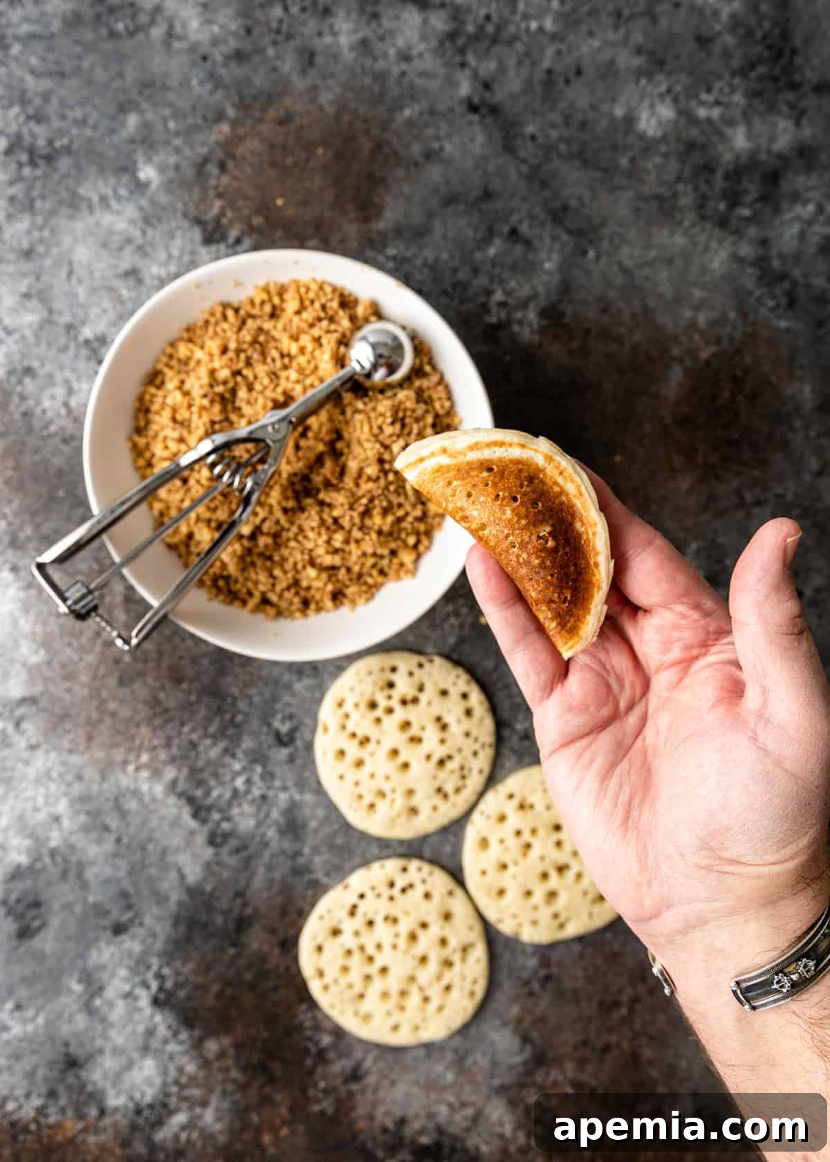 man's hand holding crescent shaped Arabic dessert pancake called a qatayef