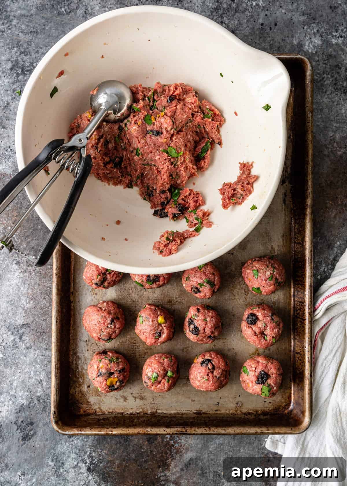 Overhead shot of a hand scooping a portion of the ground meat mixture from a large bowl, demonstrating the preparation process for forming koofteh lamb meatballs.