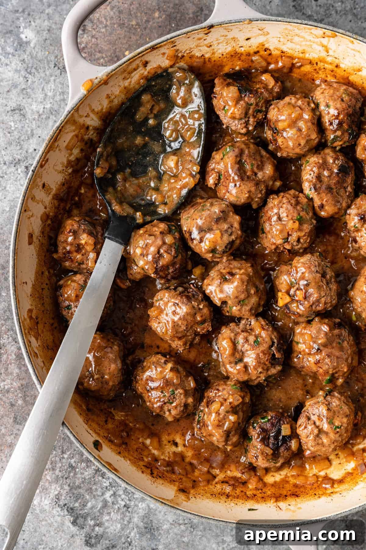 Overhead view of a serving spoon immersed in a large pot filled with Persian meatballs simmering in a rich, brown gravy, ready to be served.