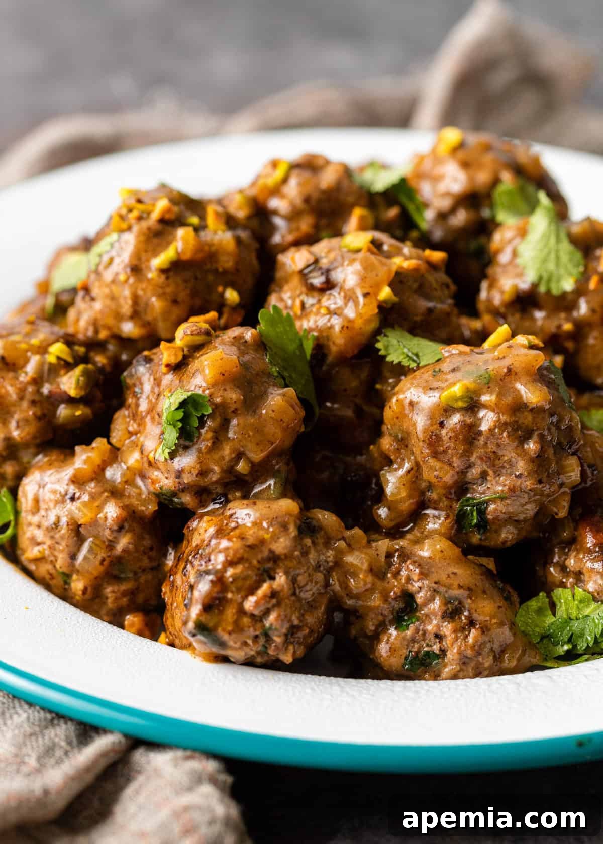 Side view of multiple koofteh (Persian meatballs) richly coated in a savory brown gravy, served elegantly in a white bowl, ready to be enjoyed.