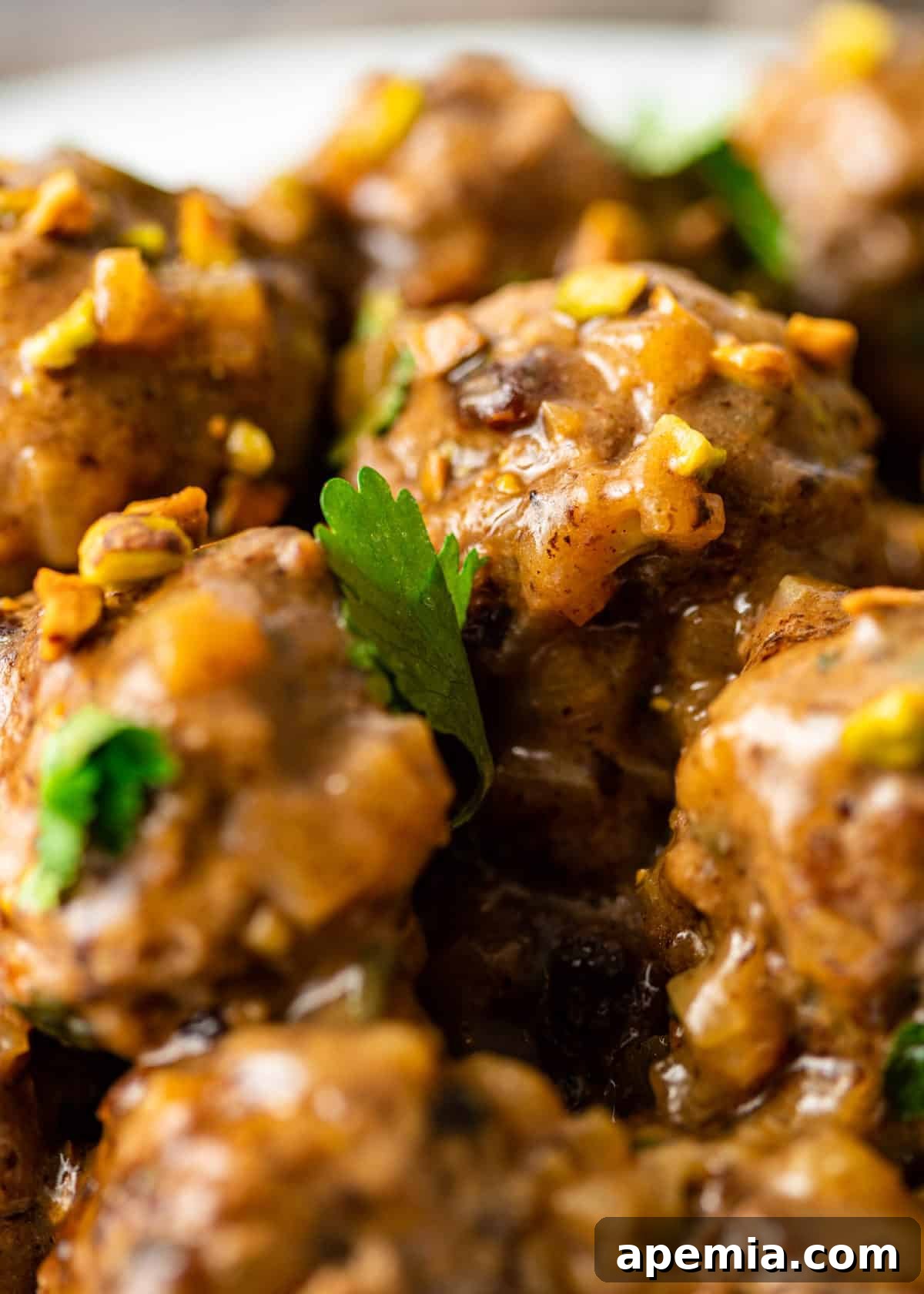 Extreme close-up view of two cooked Persian lamb meatballs, showcasing their tender texture and the slight sheen of the sauce, inviting a taste.