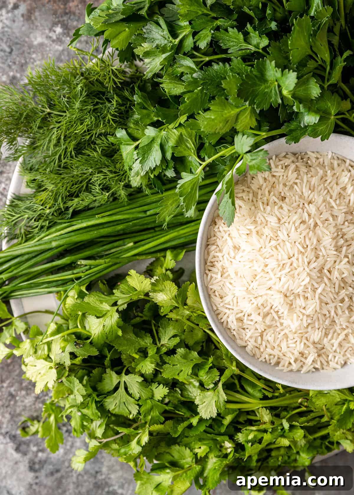 Overhead view: fresh herbs next to a small bowl of uncooked white rice, ready for preparation.