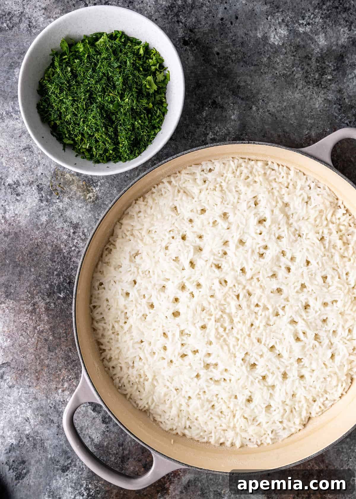 Overhead view: a bowl of finely chopped mixed herbs next to a pot of rinsed white rice, prepared for the Sabzi Polo recipe.