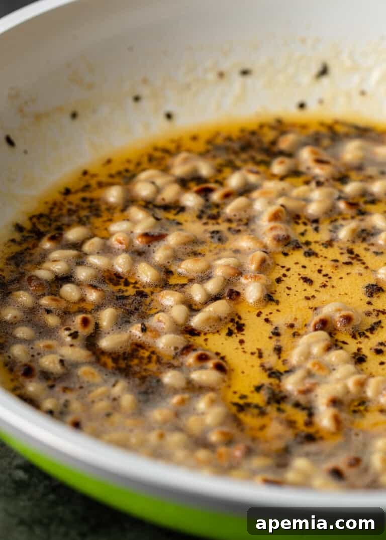 closeup: golden toasted pine nuts in a bowl, mixed with melted butter and red pepper flakes