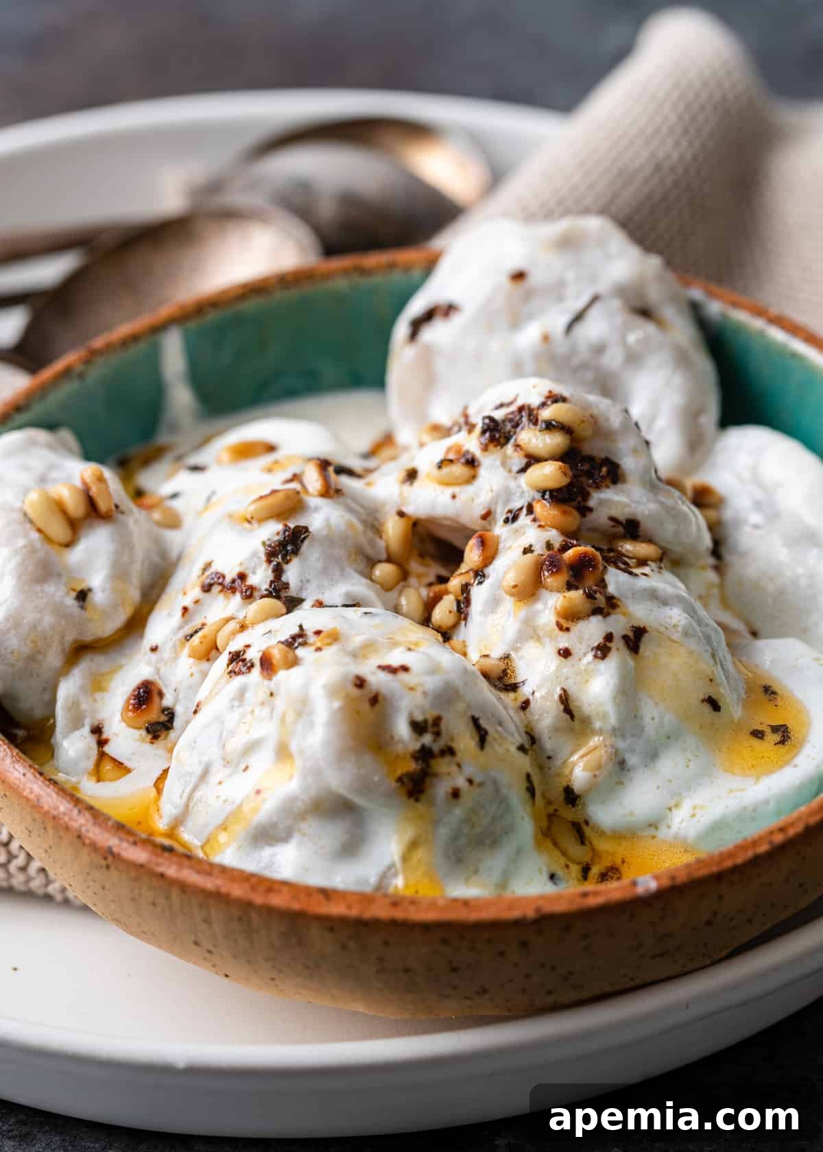 closeup: bowl with lebanese meat dumpling covered in yogurt sauce, garnished with fresh mint and pine nuts