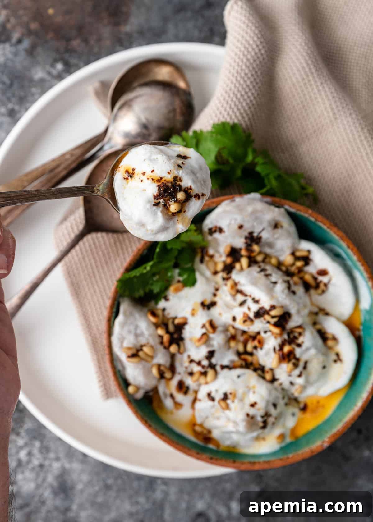 overhead lebanese meat dumpling in spoon with yogurt sauce, garnished with fresh mint