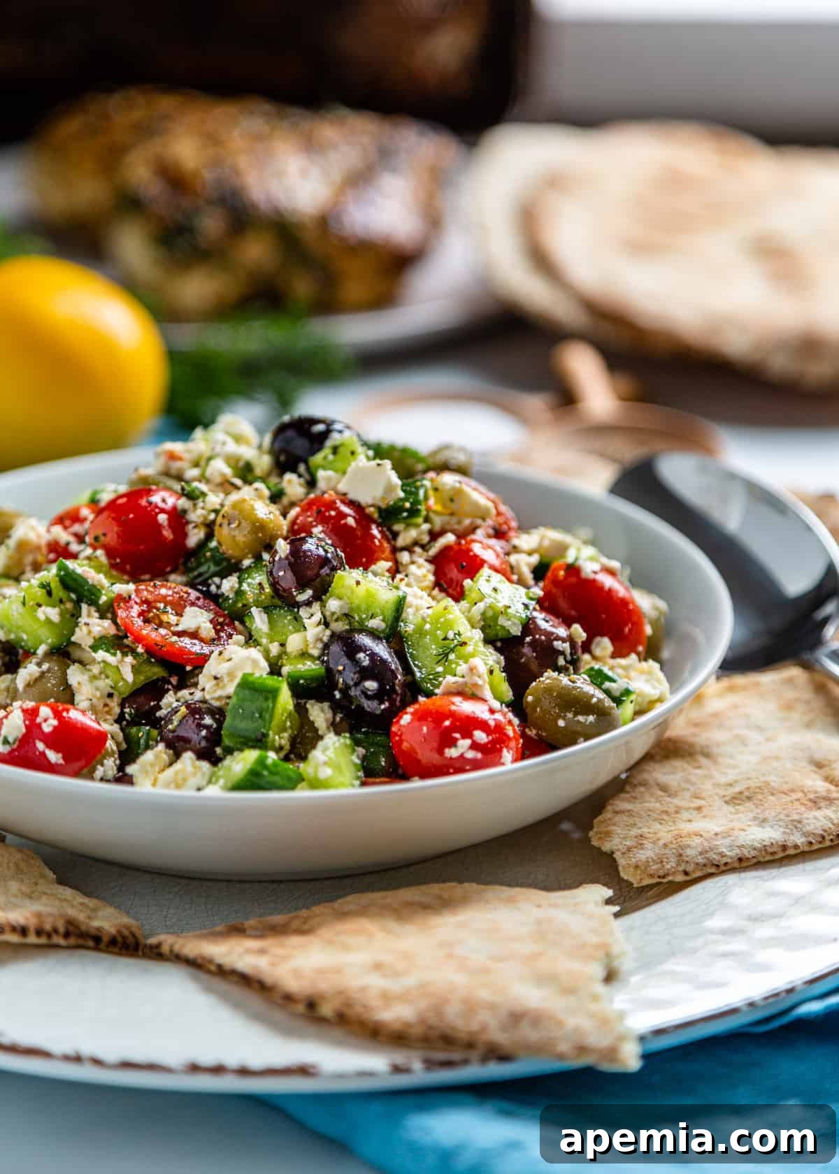 Side view of a serving of Greek Feta Salad in a white bowl with pita bread on the side