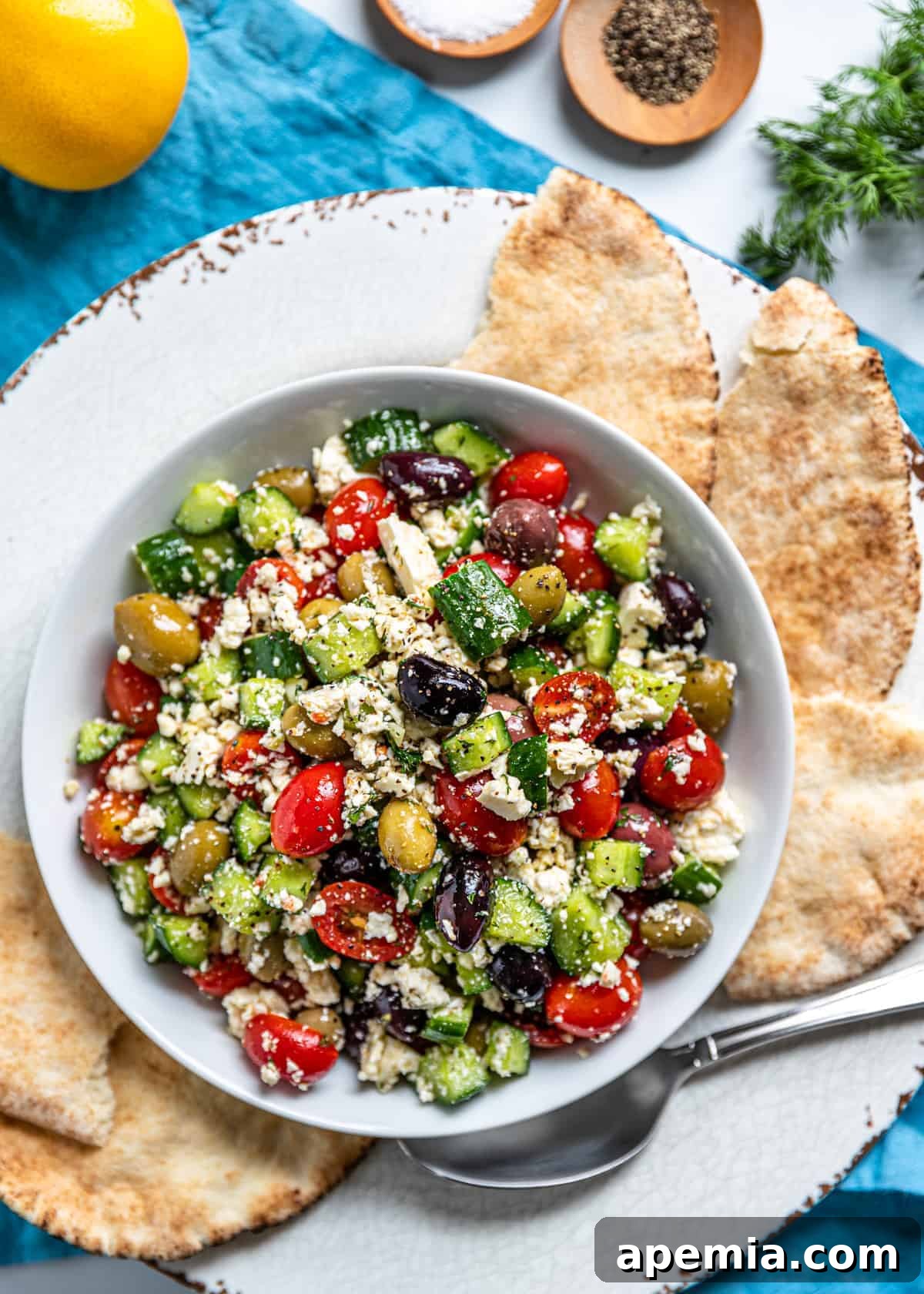 Overhead view of Greek Feta Salad with crumbled feta, olives, cucumbers, and tomatoes in a bowl with pita bread on the side
