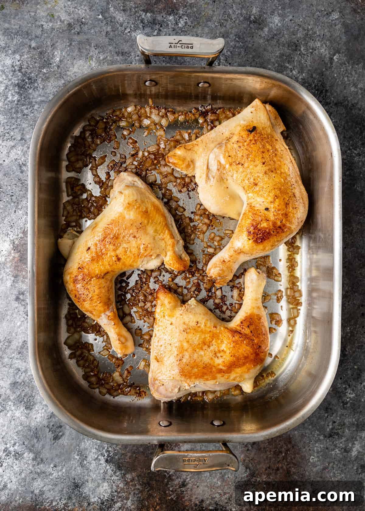 Overhead view of browned chicken thighs and legs perfectly seared in a large roasting pan, ready for baking.