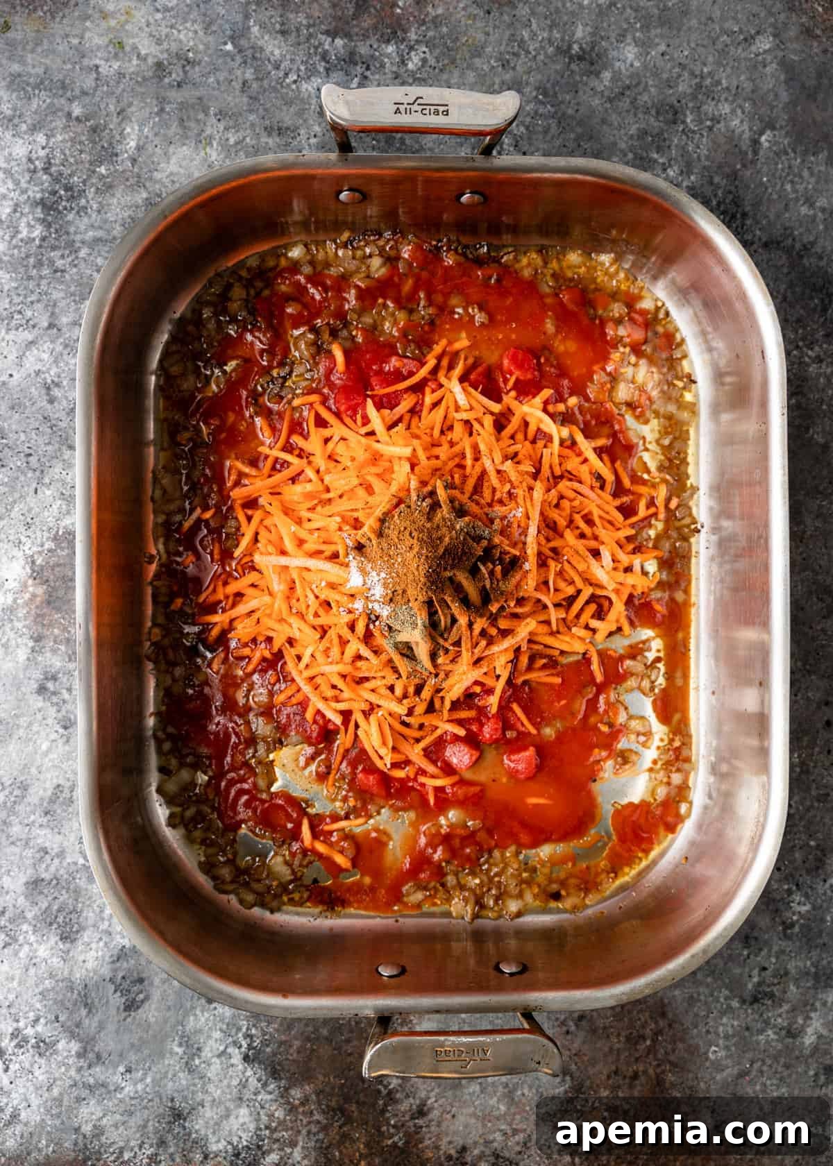 Overhead view of uncooked long-grain basmati rice mixed with rich tomato sauce and a blend of aromatic Middle Eastern spices at the bottom of a roasting pan.