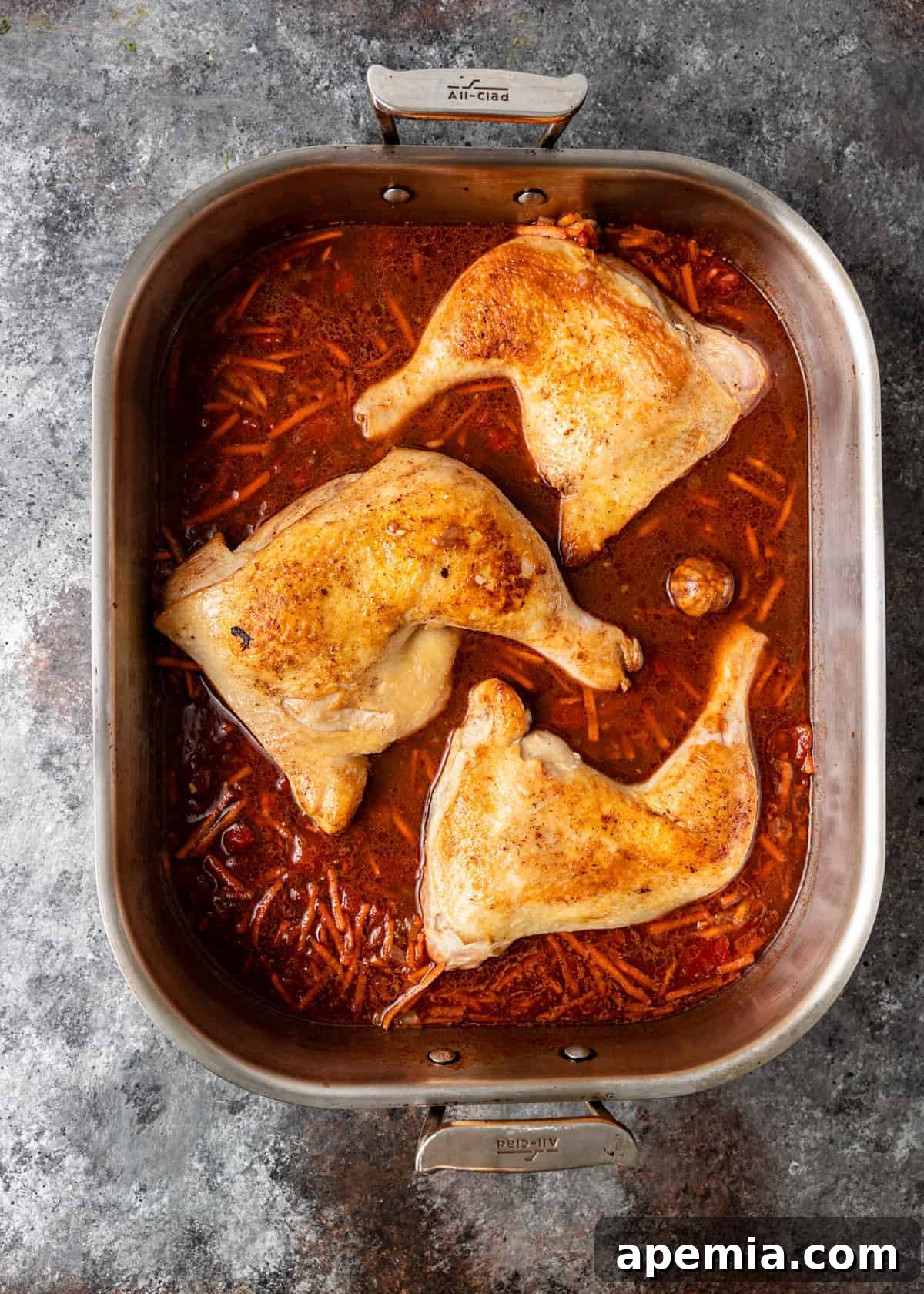 Overhead shot of perfectly pan-seared chicken quarters arranged on a bed of uncooked rice and rich tomato sauce in a large roasting pan.