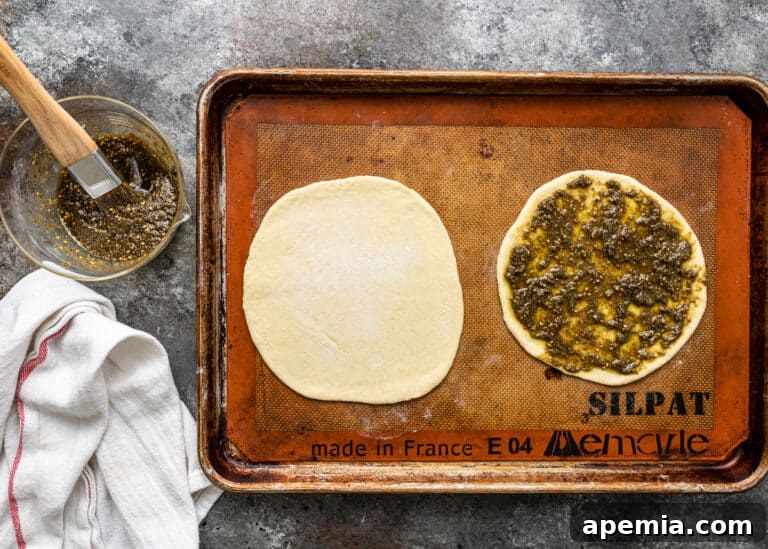 brushing olive oil and zaatar seasoning onto flatbread dough for zaatar manakish